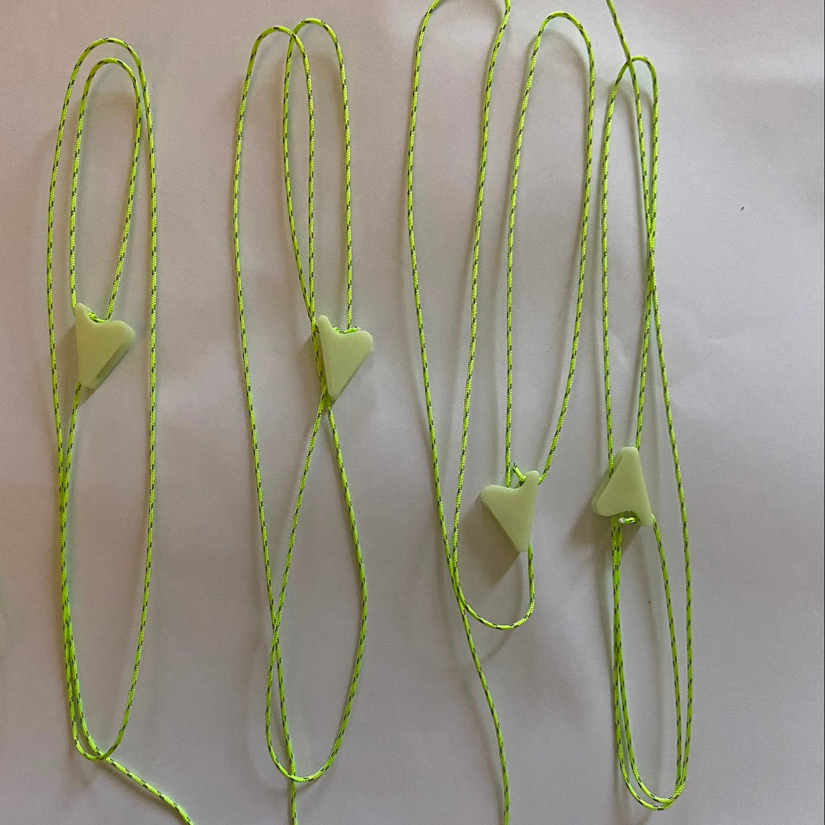 Several neon green 1mm braided guyline cords laid out on a white surface, each with a small glow in the dark line lock attached to the end