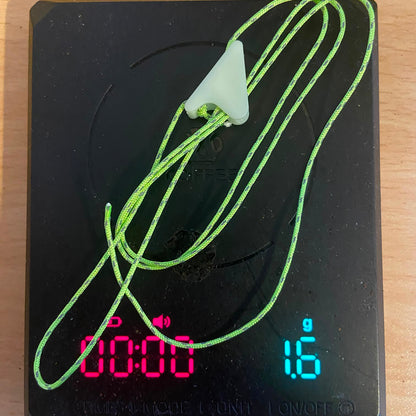 A bright green neon 1mm guyline chord placed on a digital coffee scale, showing the weight displayed as 1.6 grams on the LED display